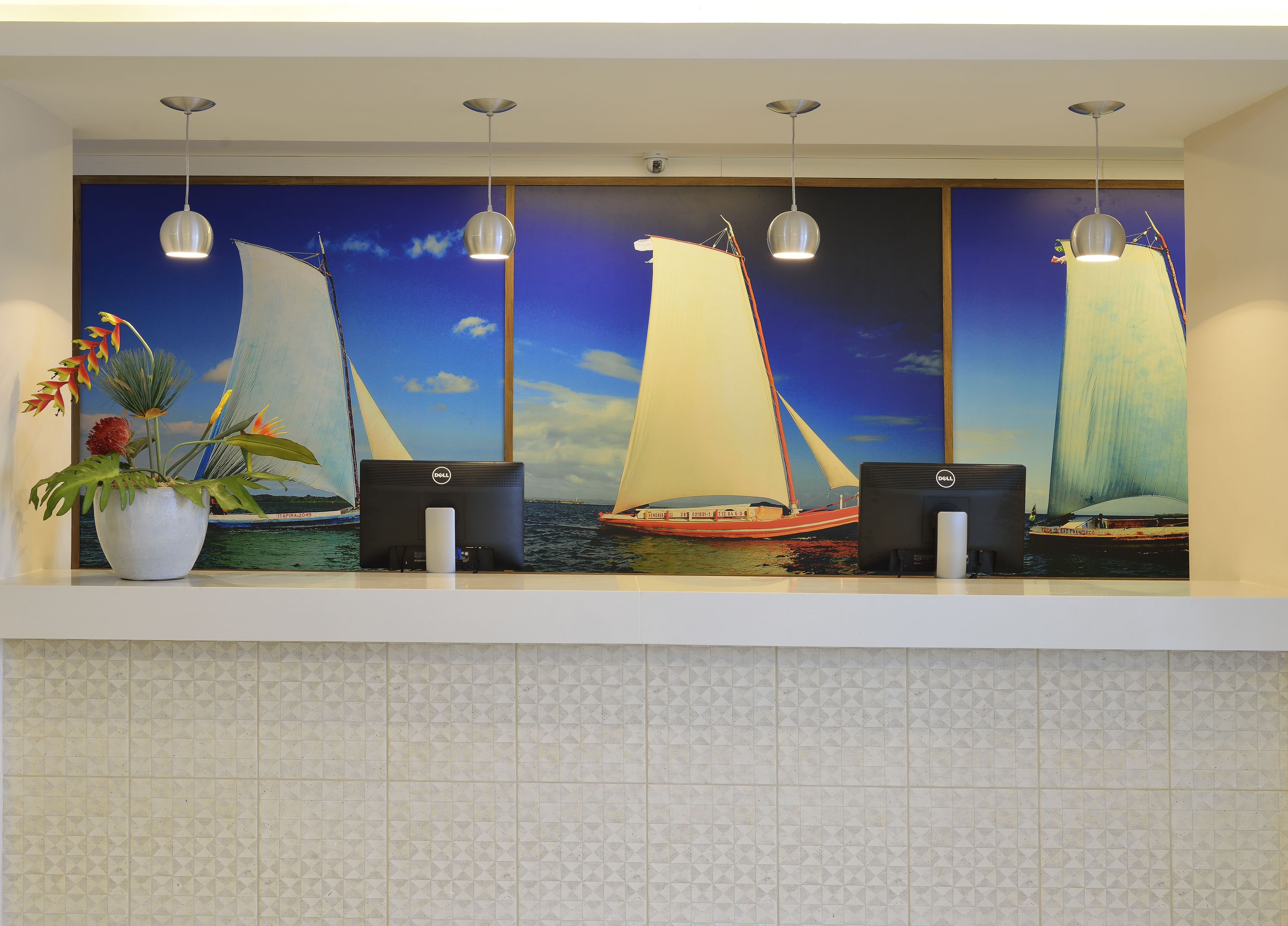 Un mostrador de recepción con un gran mural de un velero, una planta en maceta y tres luces colgantes.