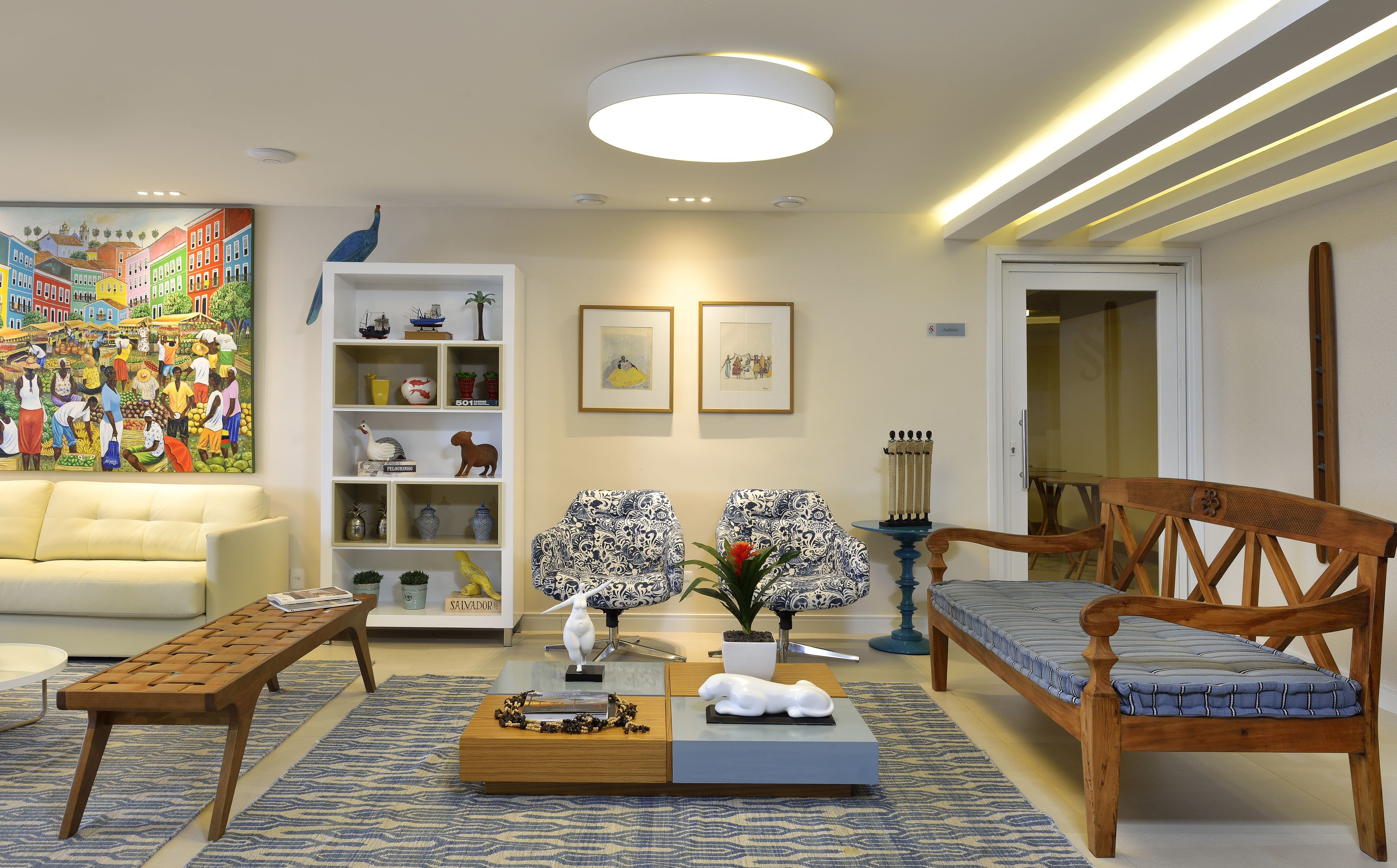 A living room with a sofa, coffee table, and chairs, a bookshelf with decorative items, and a painting on the wall.