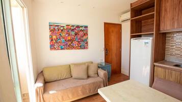 Un espacio habitable pequeño con sofá, una mesita, refrigerador y un armario de madera.