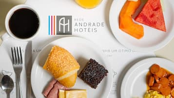 Un desayuno con diversas opciones de comida, incluyendo pan, queso, jamón, un brownie, y un plato con zanahorias en rodajas y huevos revueltos.