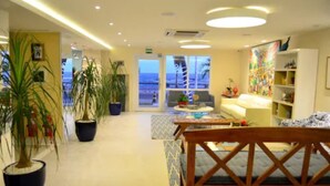 A hotel lobby with a wooden reception desk, potted plants, a sofa, and a view of the sea through large windows. - Rede Andrade Express (Salvador)