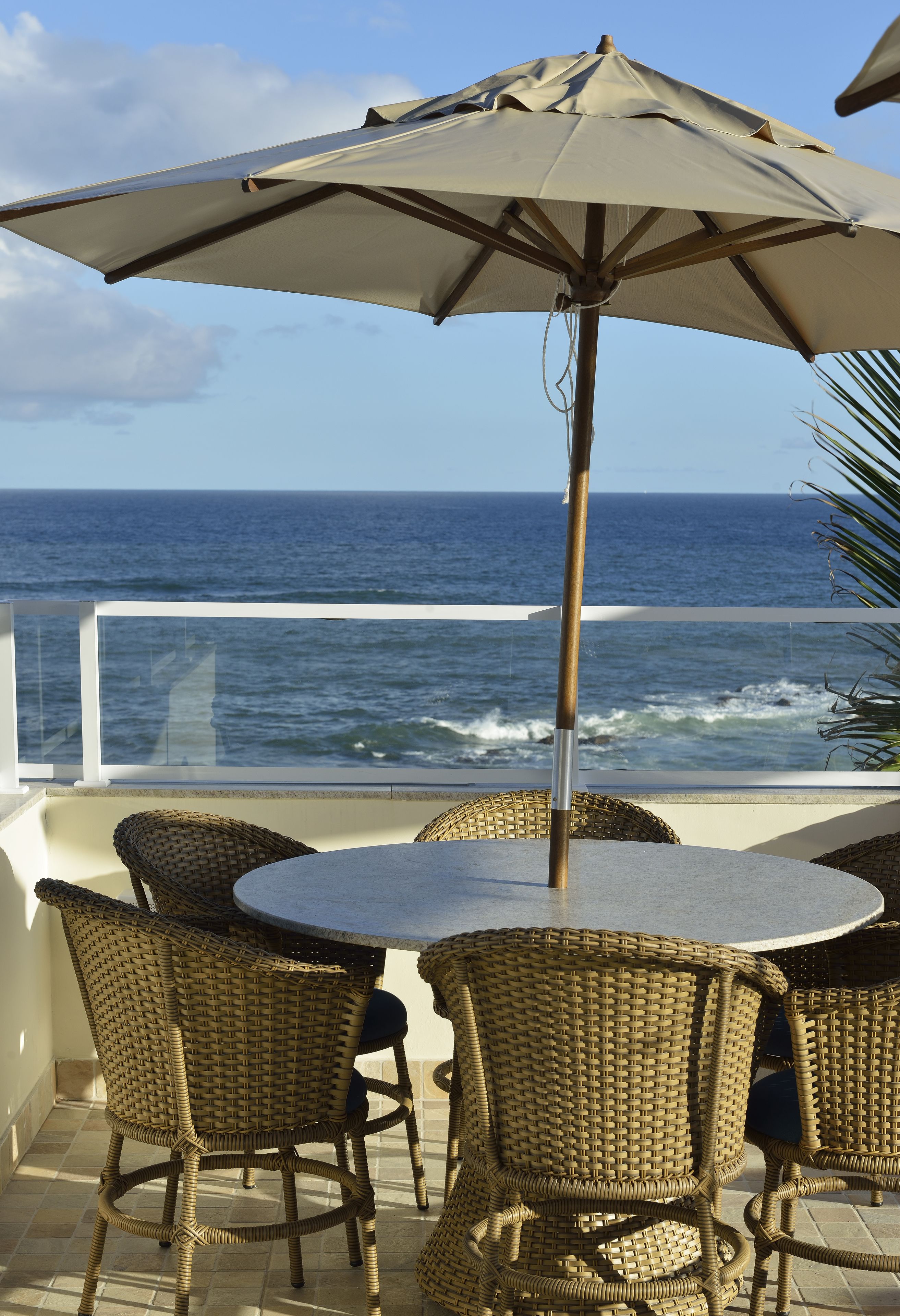 A balcony with wicker chairs and a table, overlooking the ocean.
