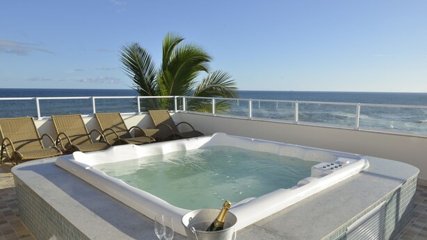 A hot tub with a champagne bottle and glasses on a balcony with a view of the ocean. - Rede Andrade Express (Salvador)