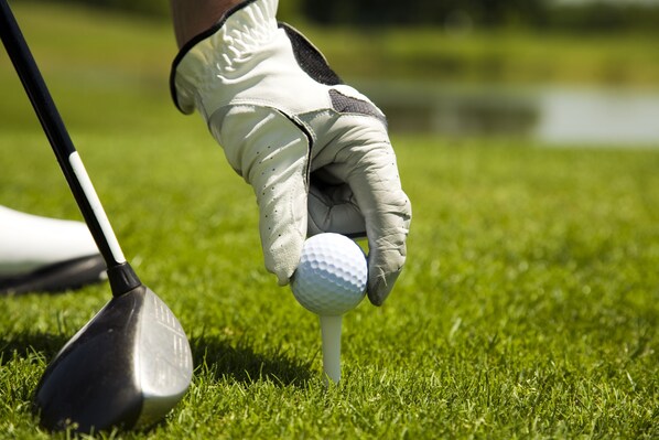 Un club de golf placé sur le gazon, avec une balle de golf posée sur un support.