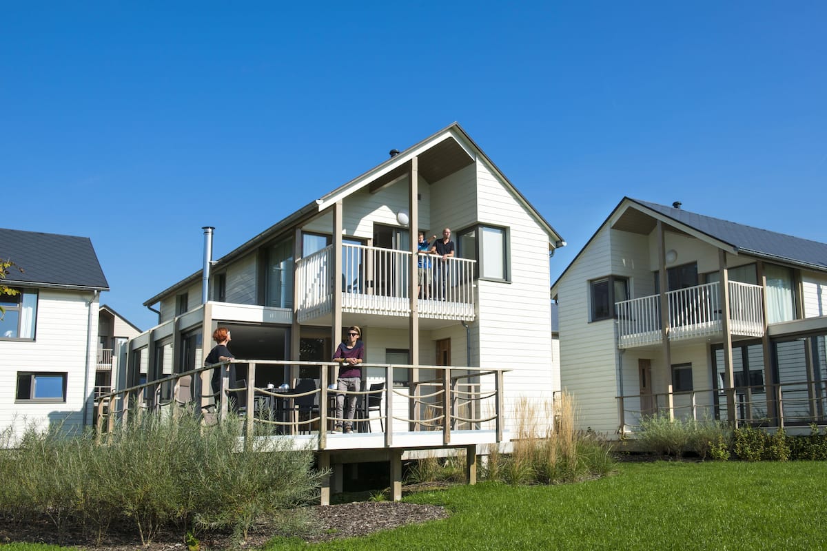 A two-story residential building with a balcony, a small deck, and a grassy yard.