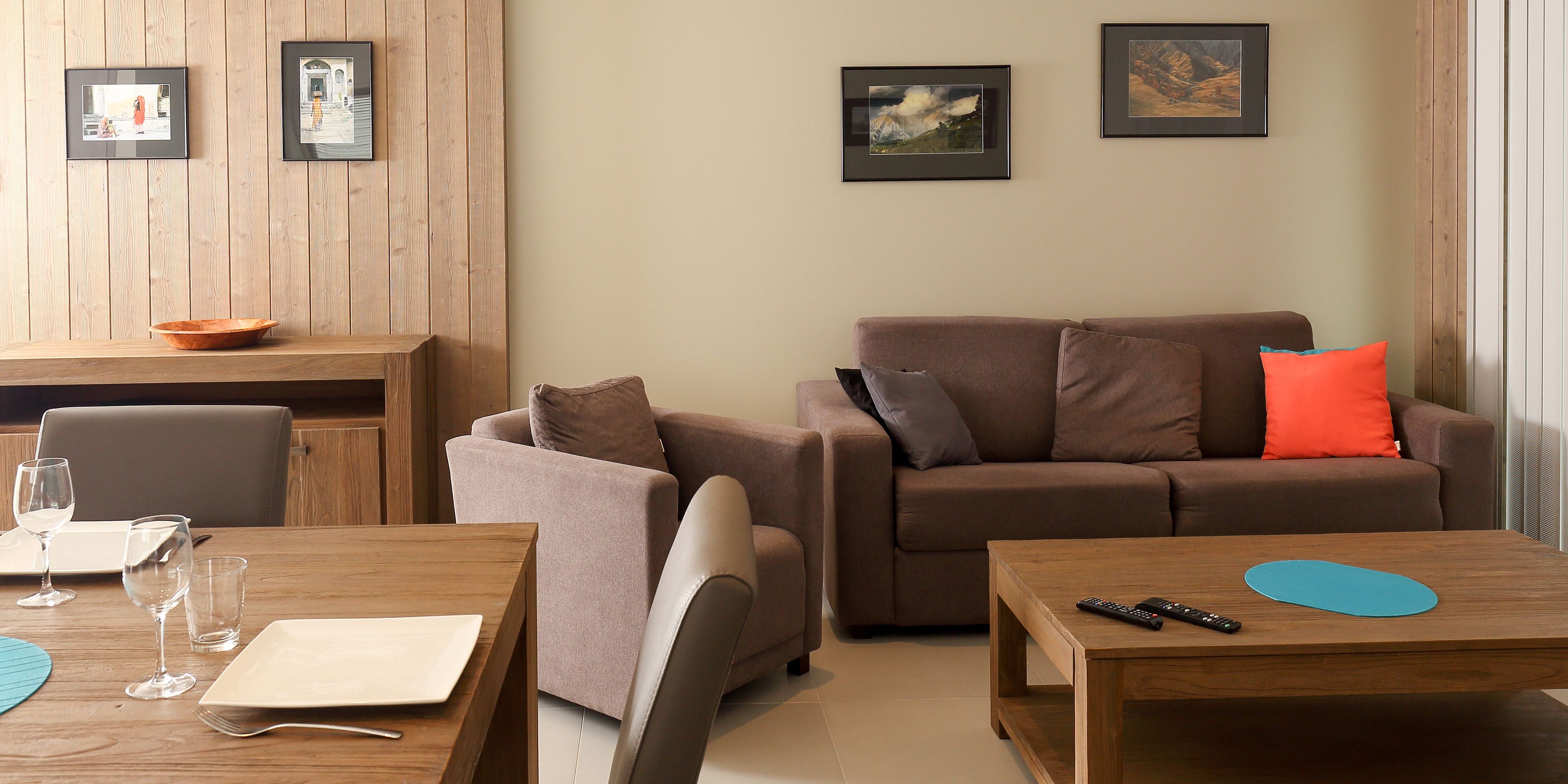 Een moderne woonkamer met een bruine bank, een houten salontafel en een eethoek met een houten tafel en stoelen.