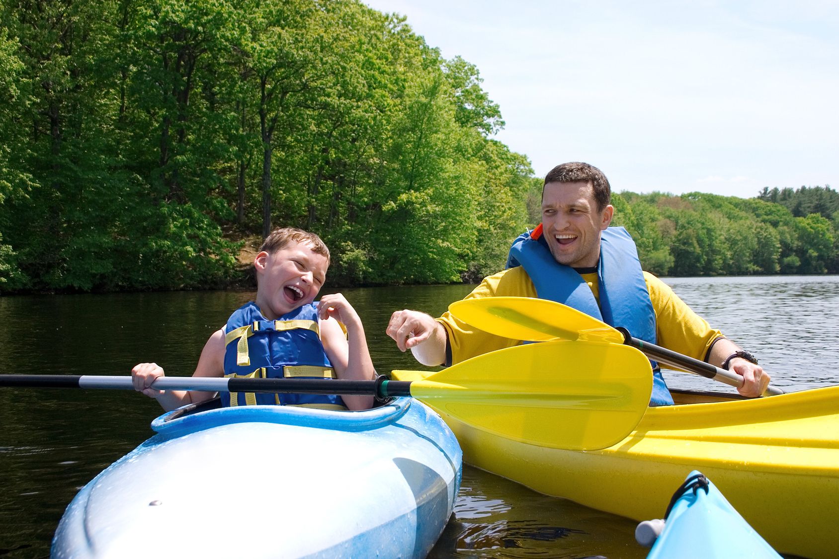 Two people in kayaks on a calm river surrounded by dense green trees.