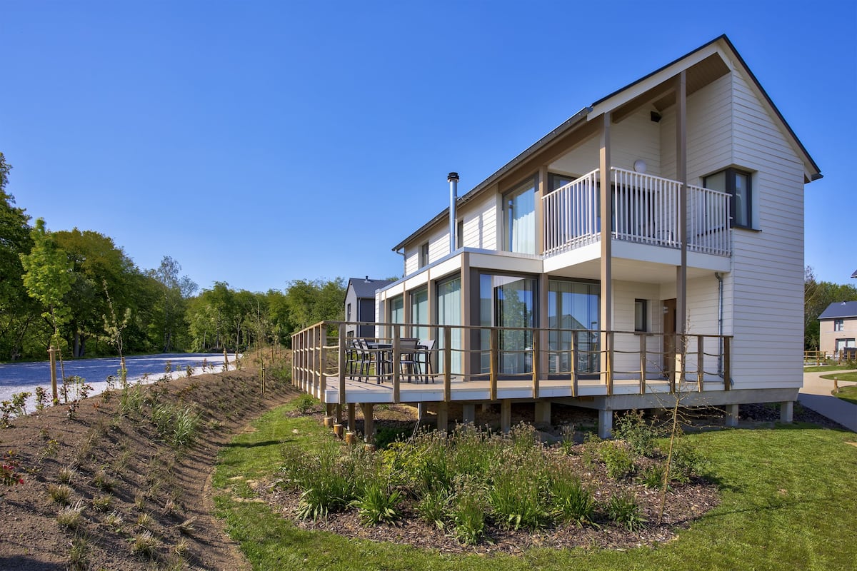 A modern two-story house with a balcony, a deck, and a view of the water.