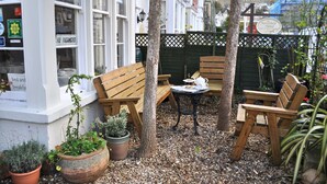 A patio with wooden benches, a small table, and potted plants. - Harringtons at Fourteen (Llandudno)