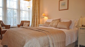 A bedroom with a large bed, a chair, a nightstand, and a lamp. - Harringtons at Fourteen (Llandudno)