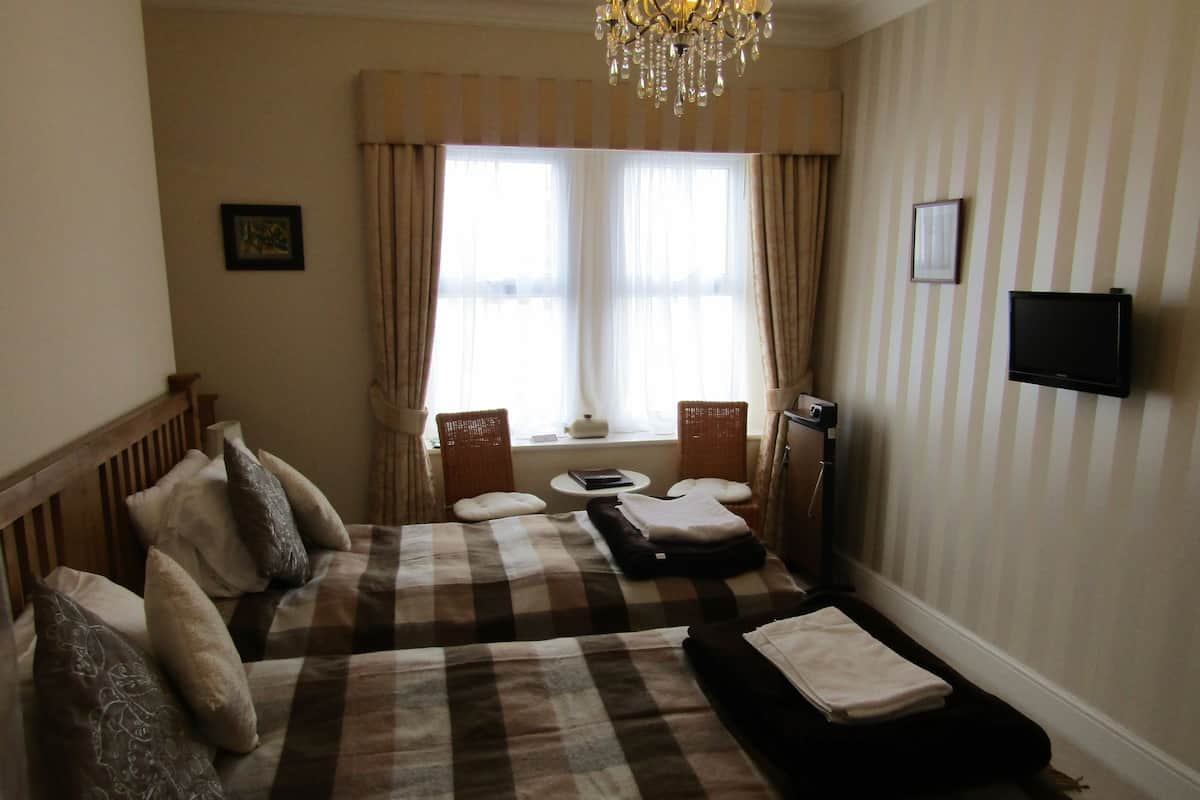 Una habitación de hotel con dos camas, televisión, ventana con cortinas, un candelabro y una pequeña mesa.