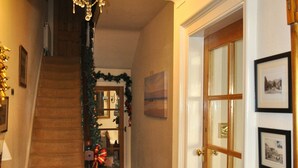 A hallway with a staircase, a chandelier, a door with glass panels, and a patterned carpet. - Harringtons at Fourteen (Llandudno)