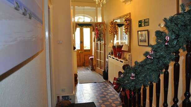 A hallway with a Christmas tree, a chandelier, and a fire exit sign. - Harringtons at Fourteen (Llandudno)