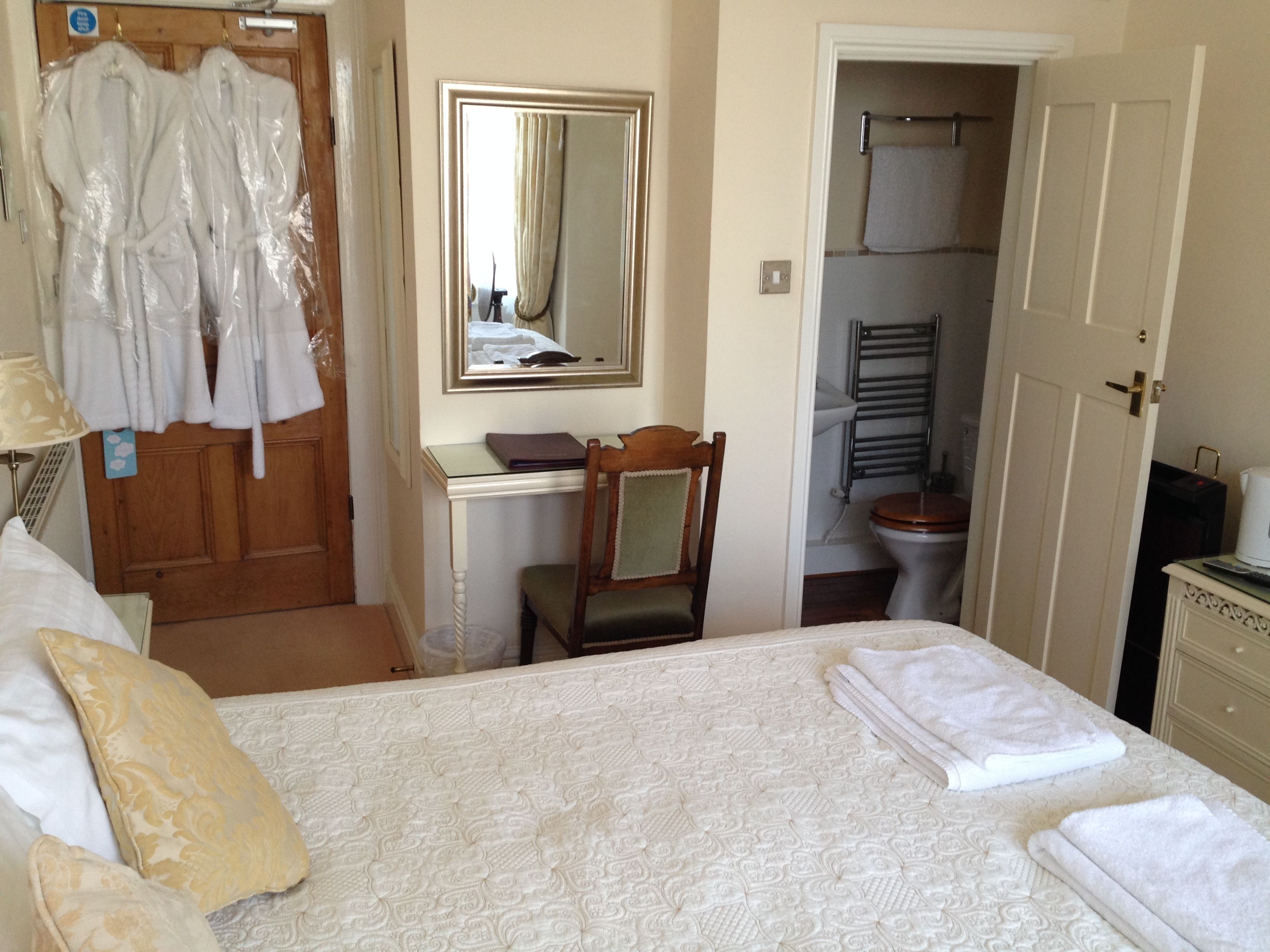 A hotel room with a bed, a desk, a chair, a wardrobe, and a bathroom visible through an open door.