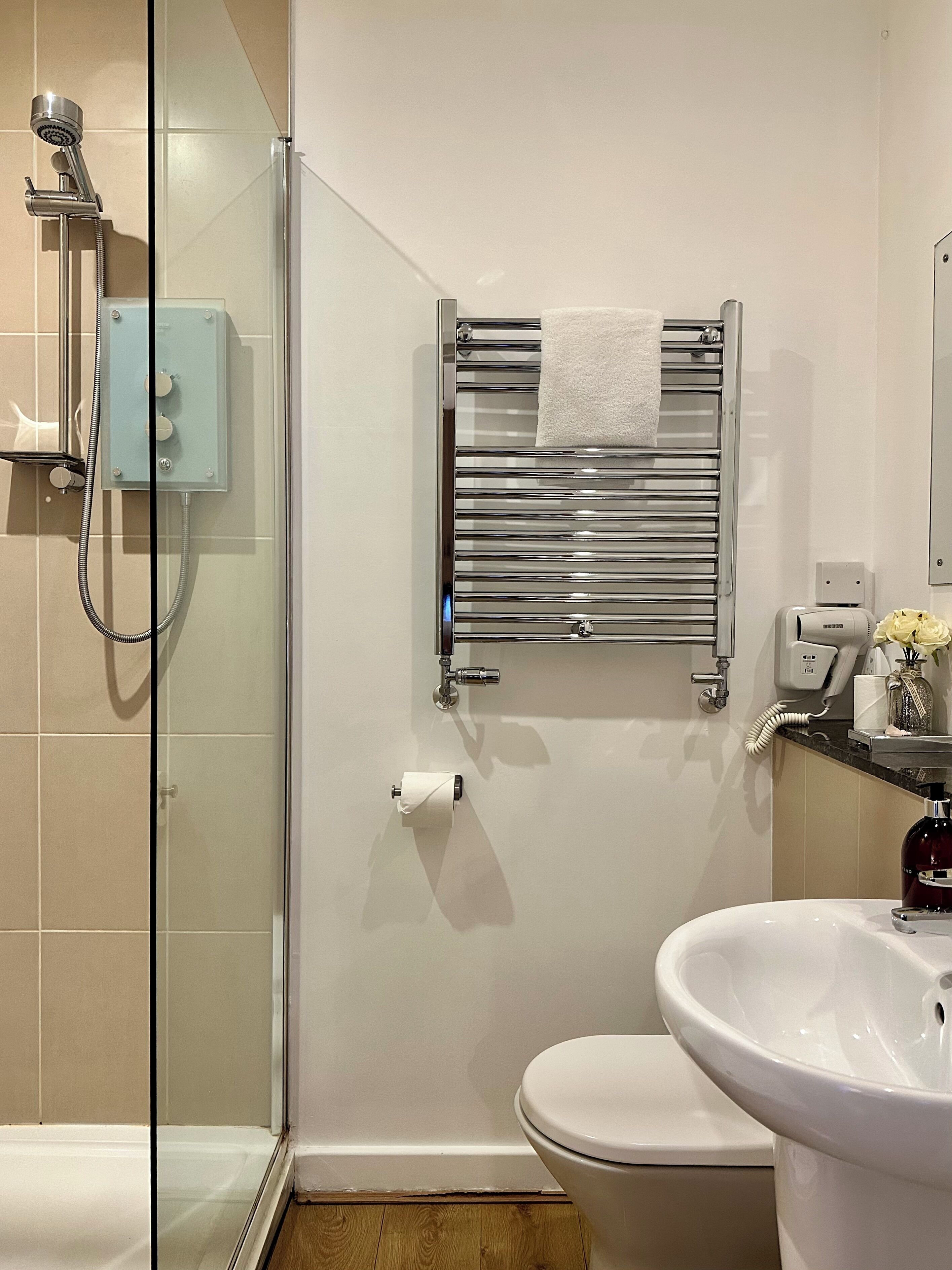 Un baño con cabina de ducha de vidrio, inodoro, lavabo y toallero con toalla.