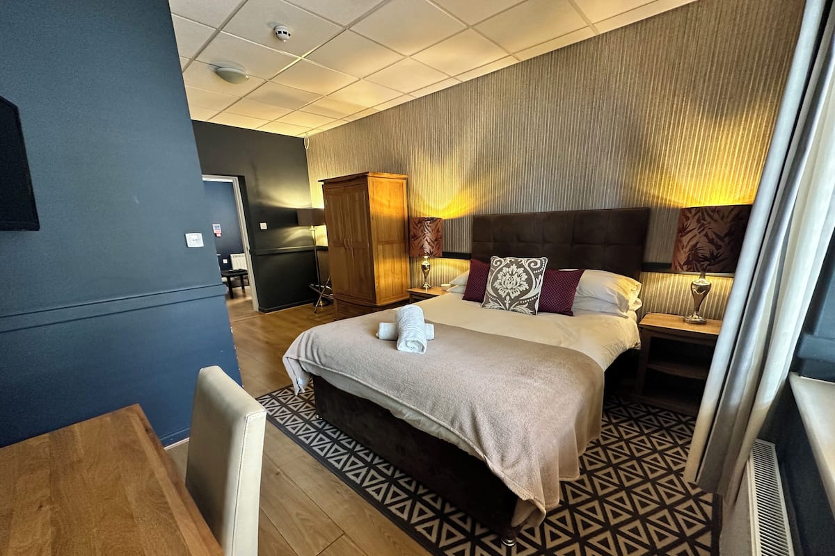 A hotel room with a large bed, a desk, a wardrobe, and a small kitchenette.