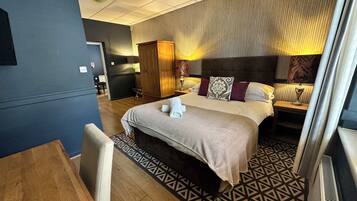 Una habitación de hotel con una cama grande, un escritorio, un armario y una pequeña cocina.
