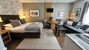 A modern hotel room with a large bed, a sofa, a small table, and a TV. - The Churchill Court (Witney)