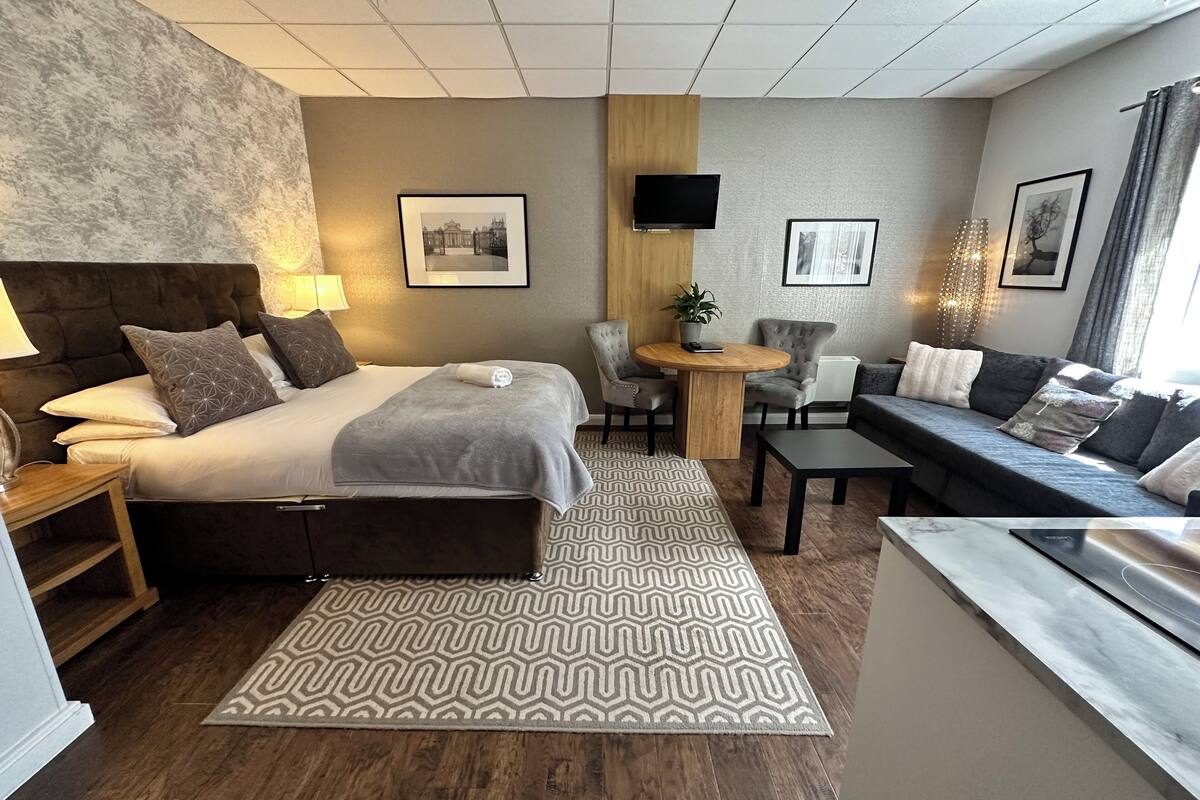 A modern hotel room with a large bed, a sofa, a small table, and a TV.