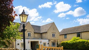 A traditional building with a stone wall, a wooden gate, and a paved driveway. - The Churchill Court (Witney)