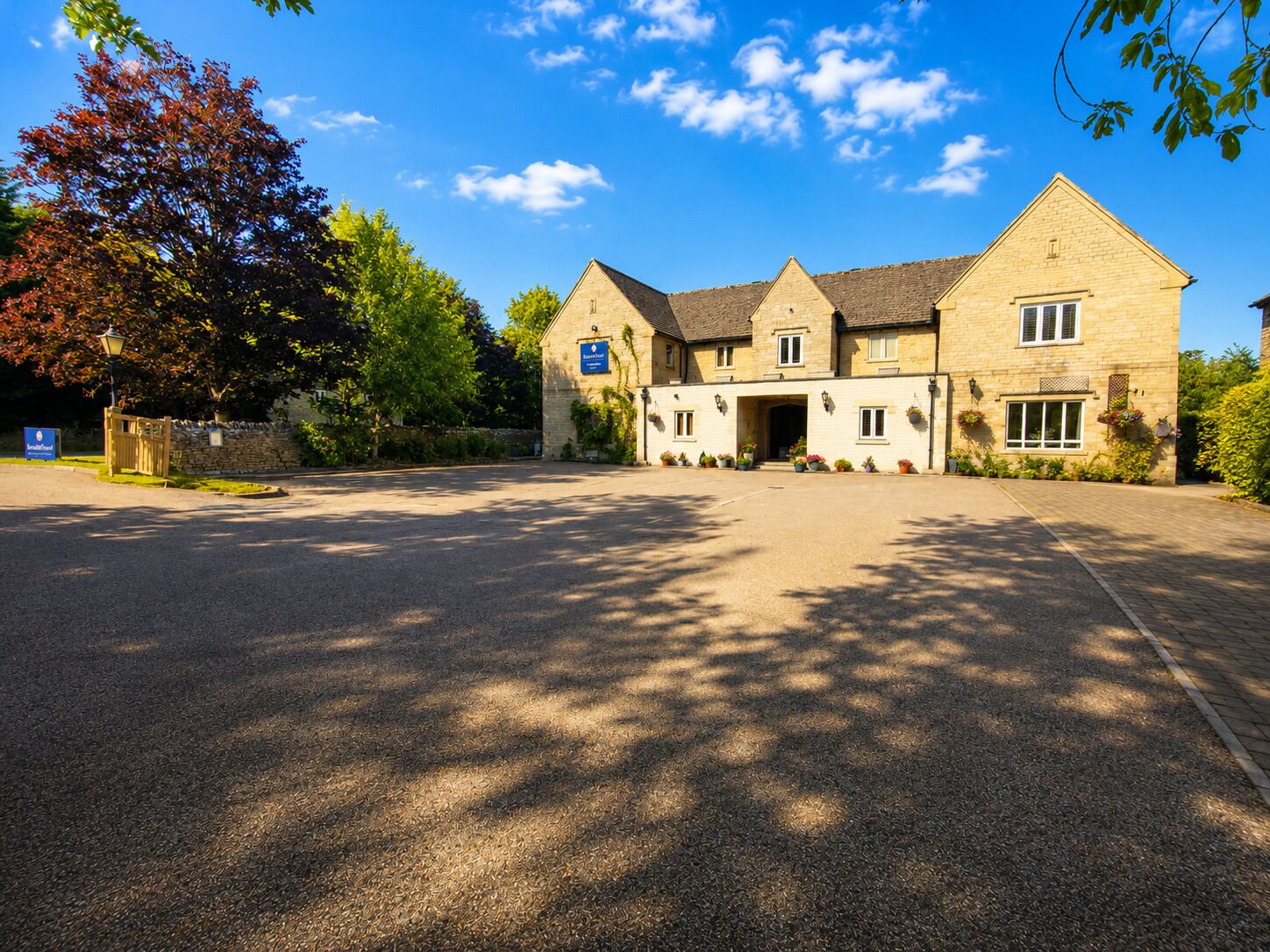 A two-story stone building with a central entrance, a paved driveway, and surrounding greenery.
