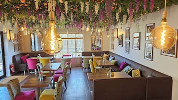 Un interior de restaurante con cabinas, mesas, lámparas colgantes y cuadros en las paredes.