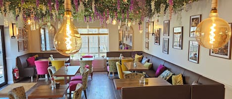 A restaurant interior with booths, tables, hanging light fixtures, and framed artwork on the walls.