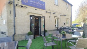 Churchill Court with outdoor seating and a sign indicating rooms, suites, café, and short-term lets. - The Churchill Court (Witney)