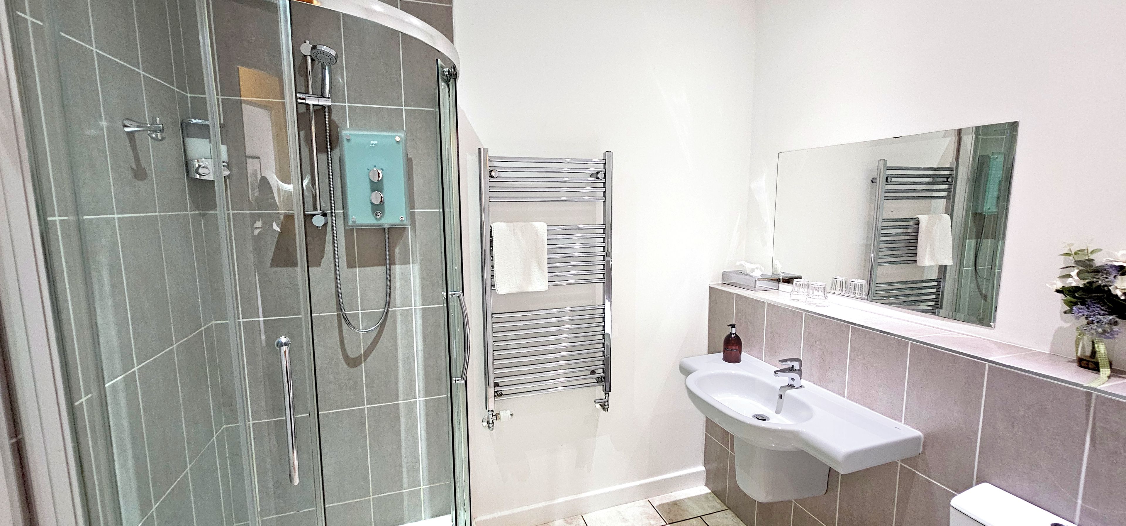 Un baño moderno con ducha acristalada, lavamanos blanco y perchero para toallas.