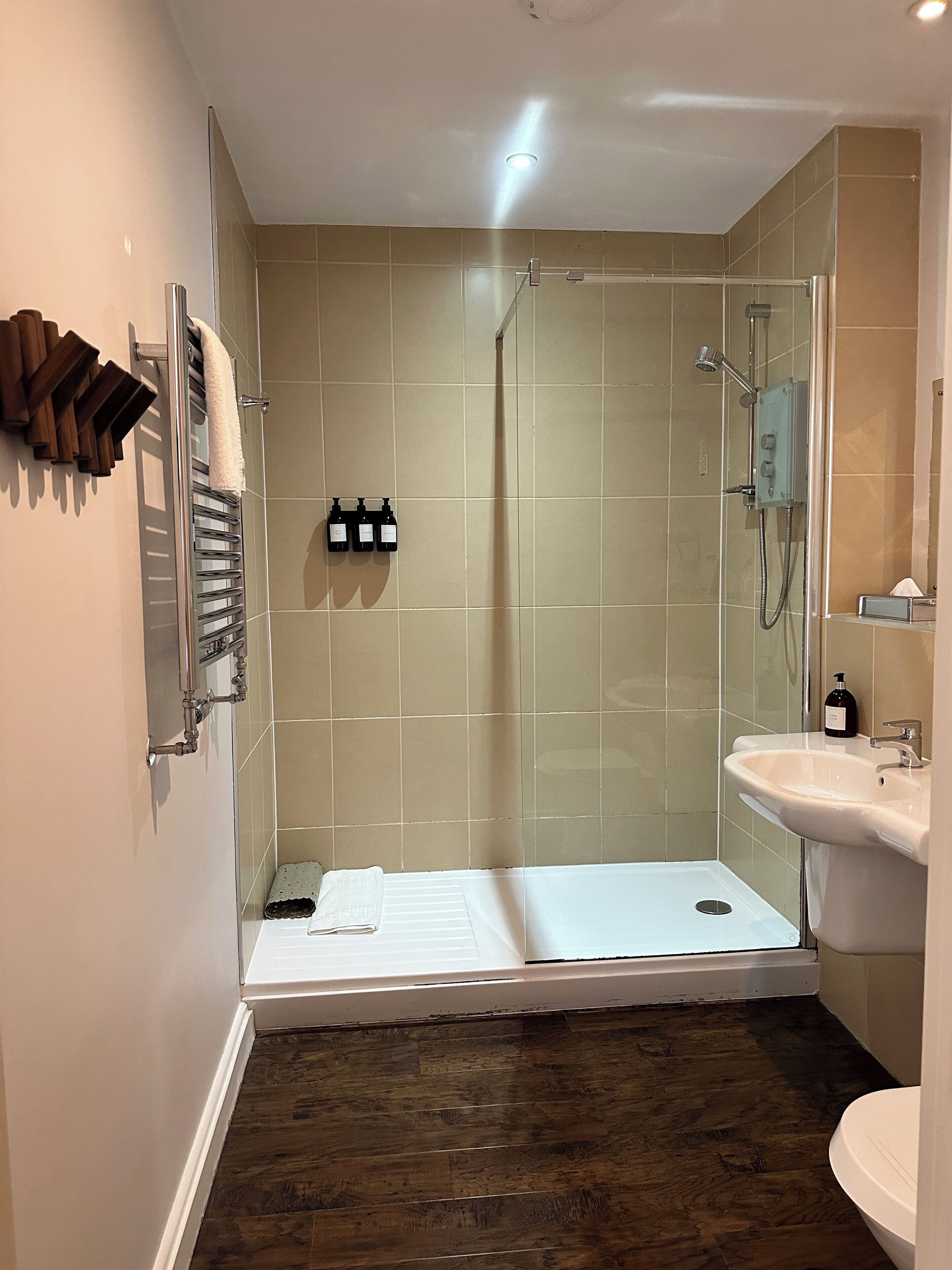 Ein modernes Badezimmer mit einer Duschkabine, einem weißen Waschbecken und einem Holzhandtuchhalter.