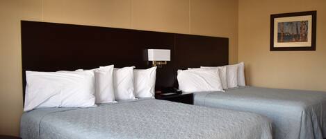 A hotel room with two beds, a nightstand, a lamp, and a framed picture on the wall.