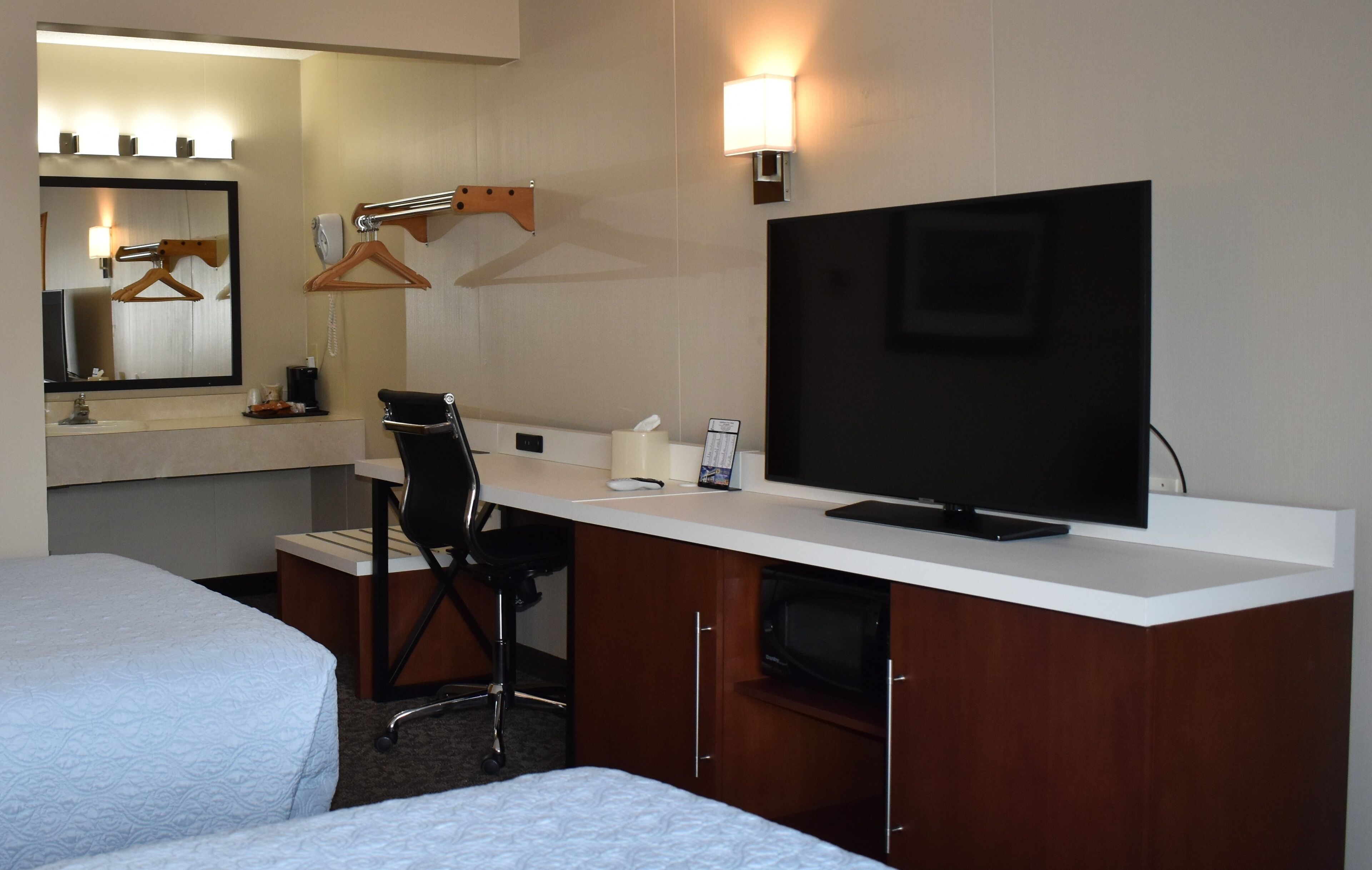 Habitación de hotel con dos camas, un escritorio con televisor, una silla, una lámpara de escritorio, un teléfono y un espejo.