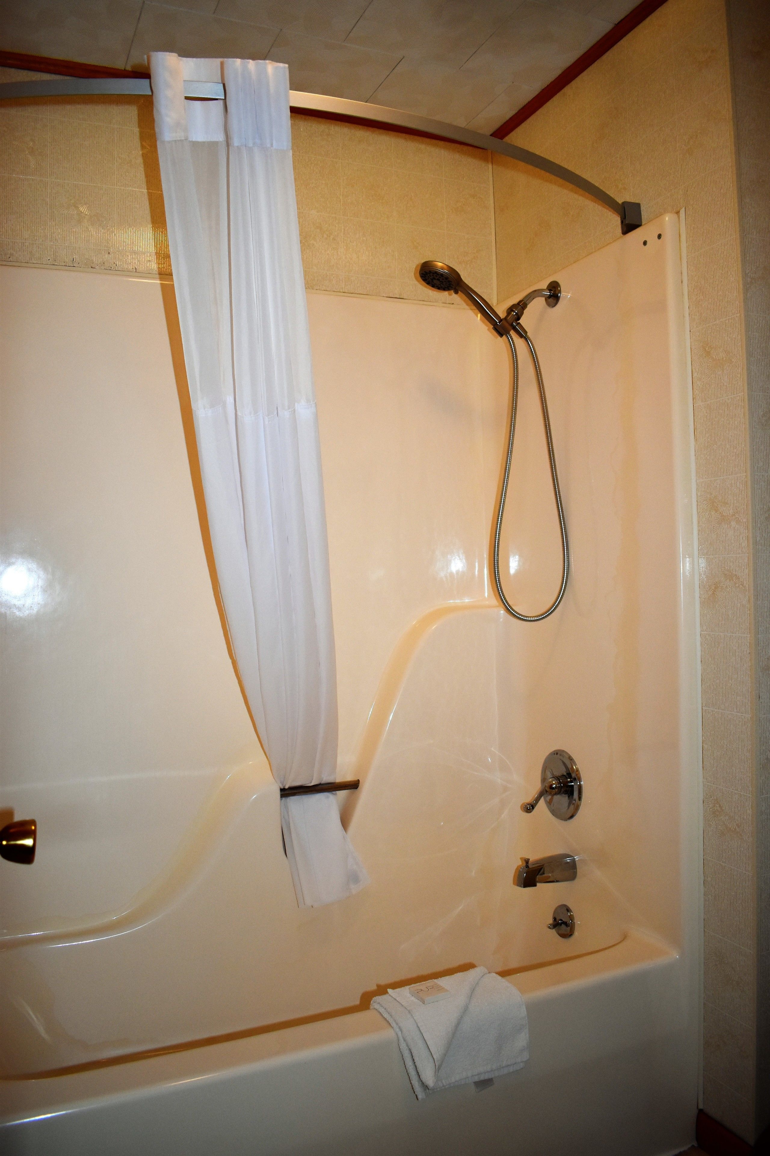 A white bathtub with a shower head and faucet, a towel hanging on the side, and a curtain.