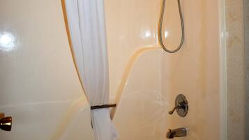 A white bathtub with a shower head and faucet, a towel hanging on the side, and a curtain.