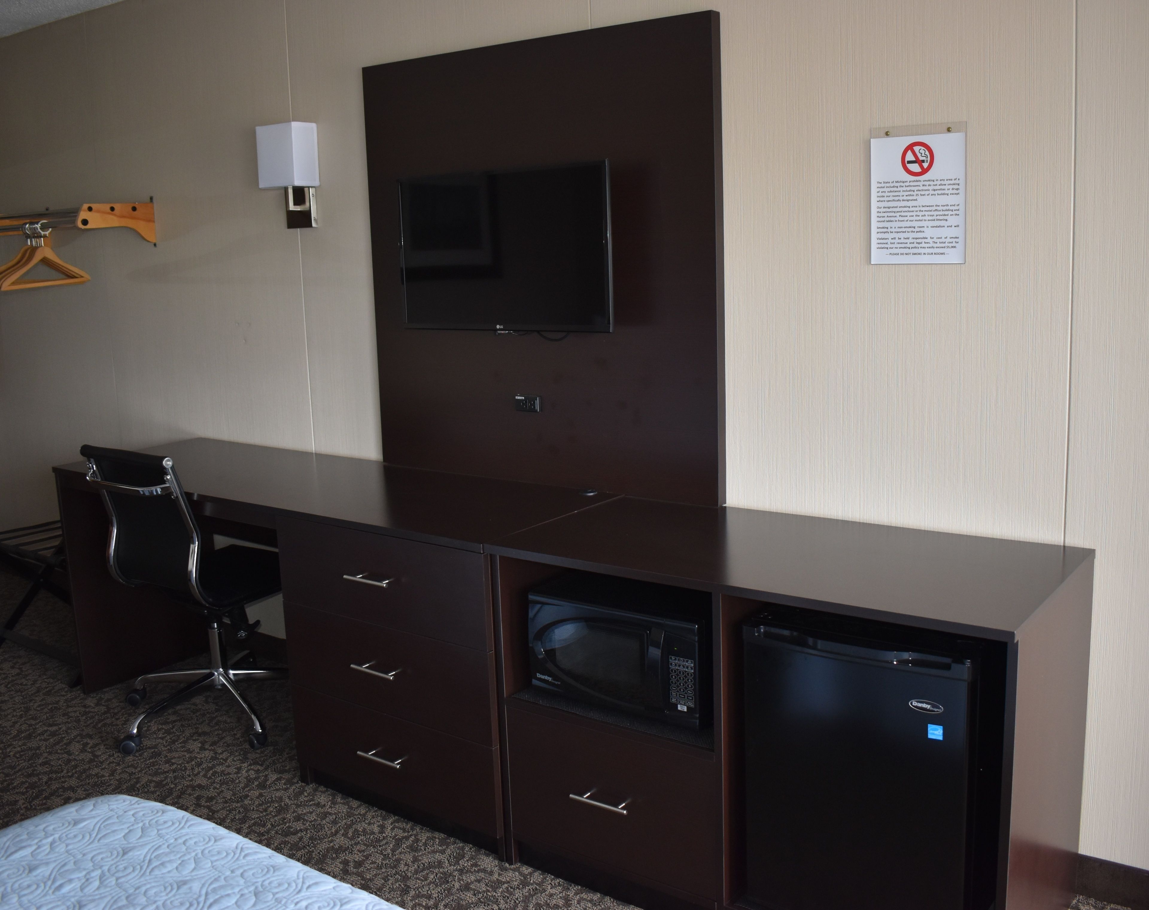 A hotel room with a dark wooden desk, a flat-screen TV, a microwave, and a mini-fridge.