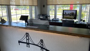 A reception desk with a 'NO PETS ALLOWED' sign, a computer, a telephone, and a view of a bridge through the window. - Lighthouse View Motel (Mackinaw City)