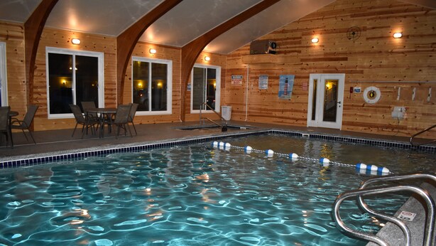 An indoor swimming pool with clear water, wooden walls, and a seating area with chairs. - Lighthouse View Motel (Mackinaw City)