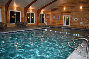 Une piscine intérieure à l’eau claire, avec des murs en bois et un espace détente équipé de chaises.