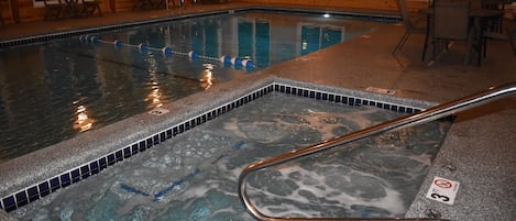 En swimmingpool med ett område för bubbelbad, trädäckstolar och ett kaklat trädäck.