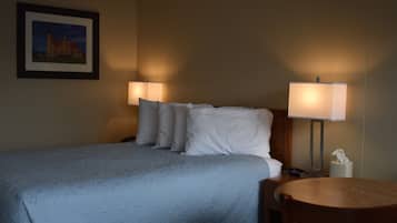 A hotel room with a bed, two bedside lamps, a round wooden table, and a framed picture on the wall.
