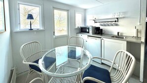 Una cocina compacta equipada con microondas, cafetera y un lavamanos pequeño. Hay una mesa de comedor con sillas y una ventana con vistas a árboles.