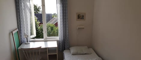 Een kleine, net kamer met een enkel bed, een bureau met stoel en een raam met gordijnen met dessin.