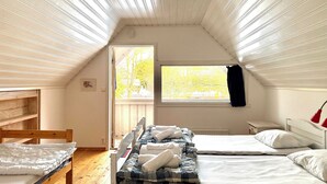Un dormitorio ático acogedor con dos camas, una ventana con vista a árboles, una silla de madera y una mesita.