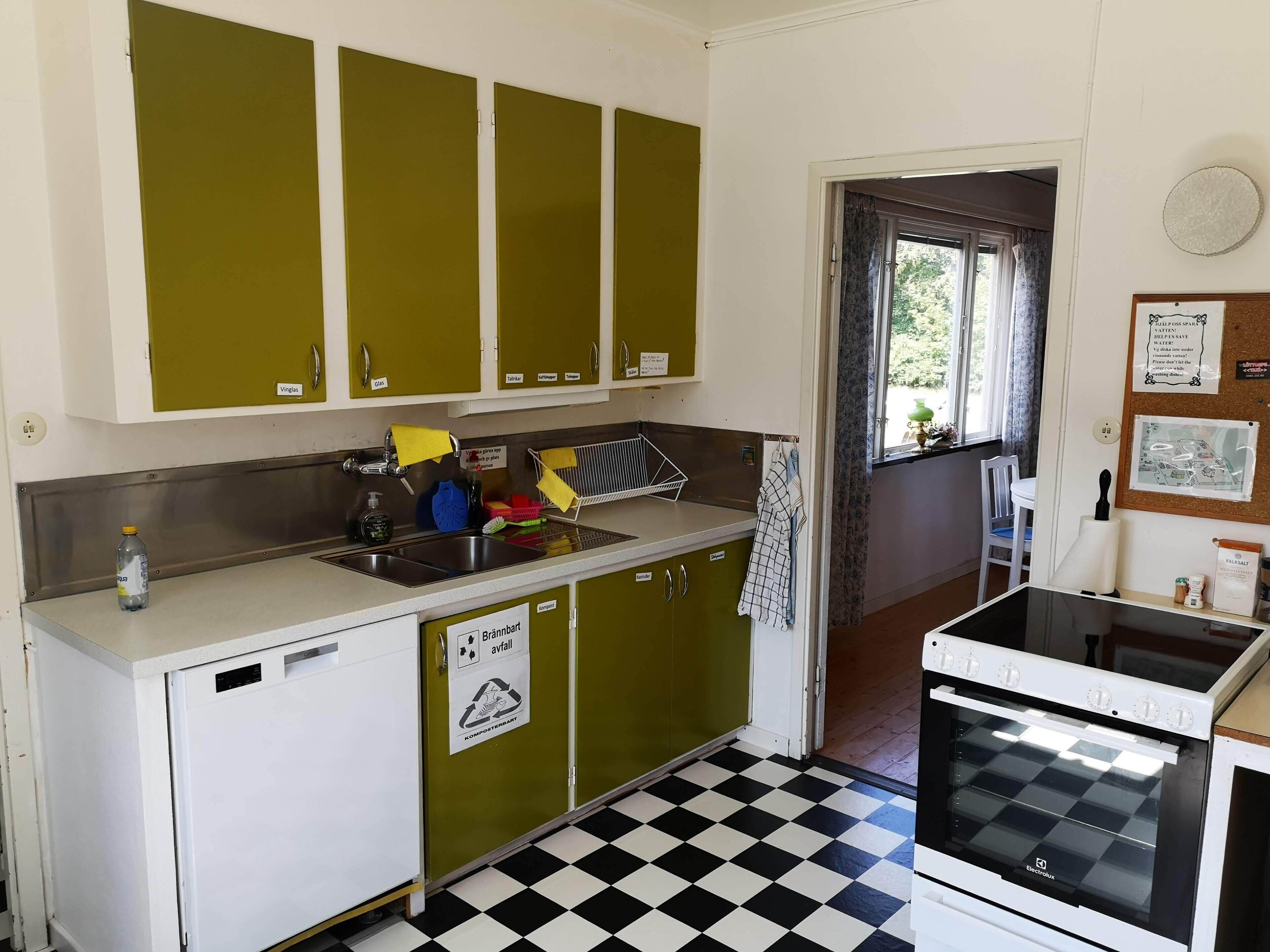 A compact kitchen with green cabinets, a white countertop, a black and white checkered floor, and a white oven.