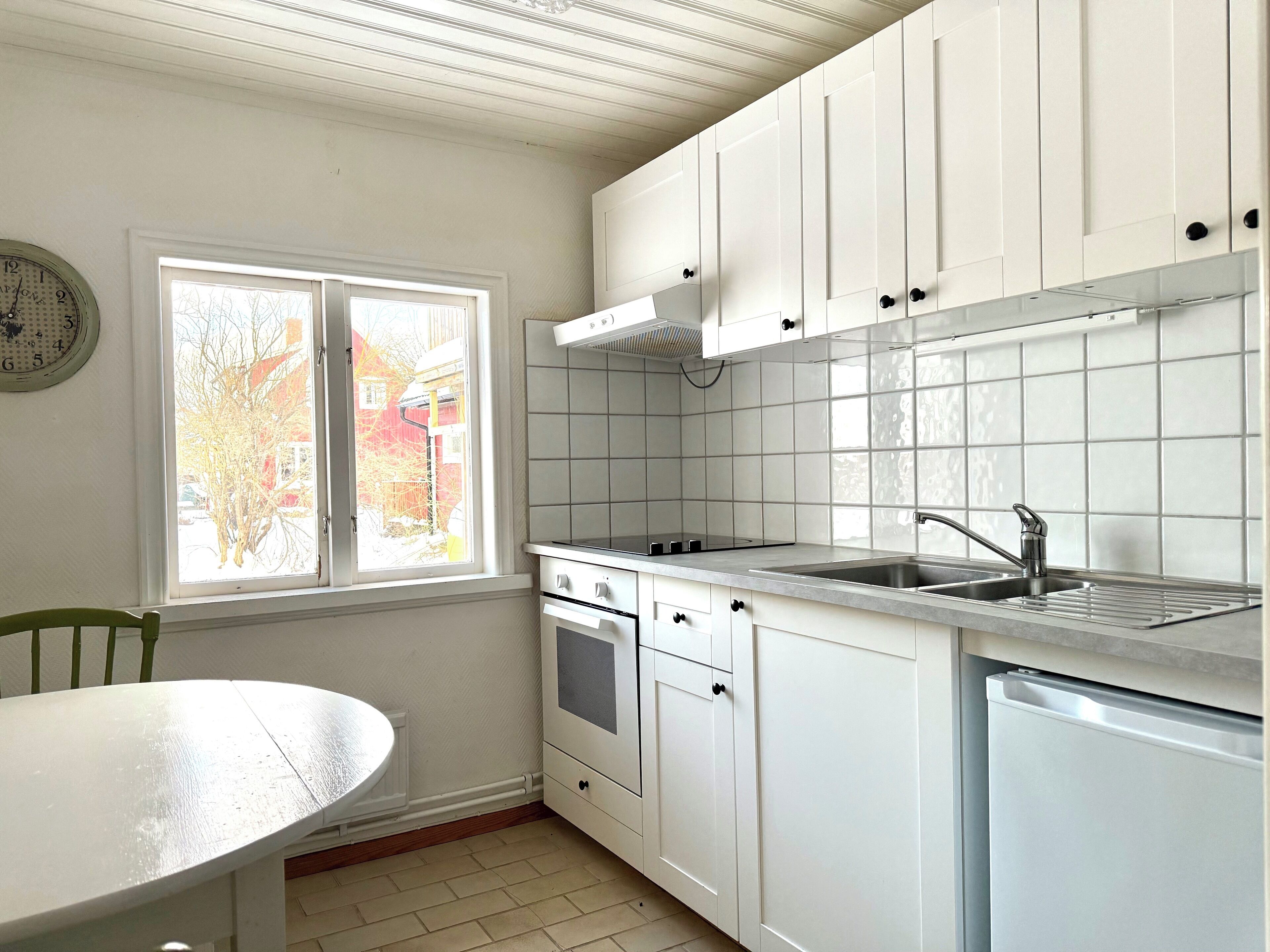 A kitchen with white cabinets, a stainless steel sink, and a window with a view of a red building.