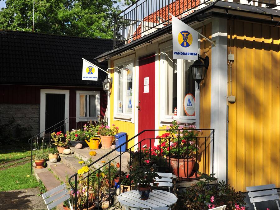 Ein gelbes Gebäude mit rotem Eingang, einem Balkon und Außenbereich mit Stühlen und Tischen.