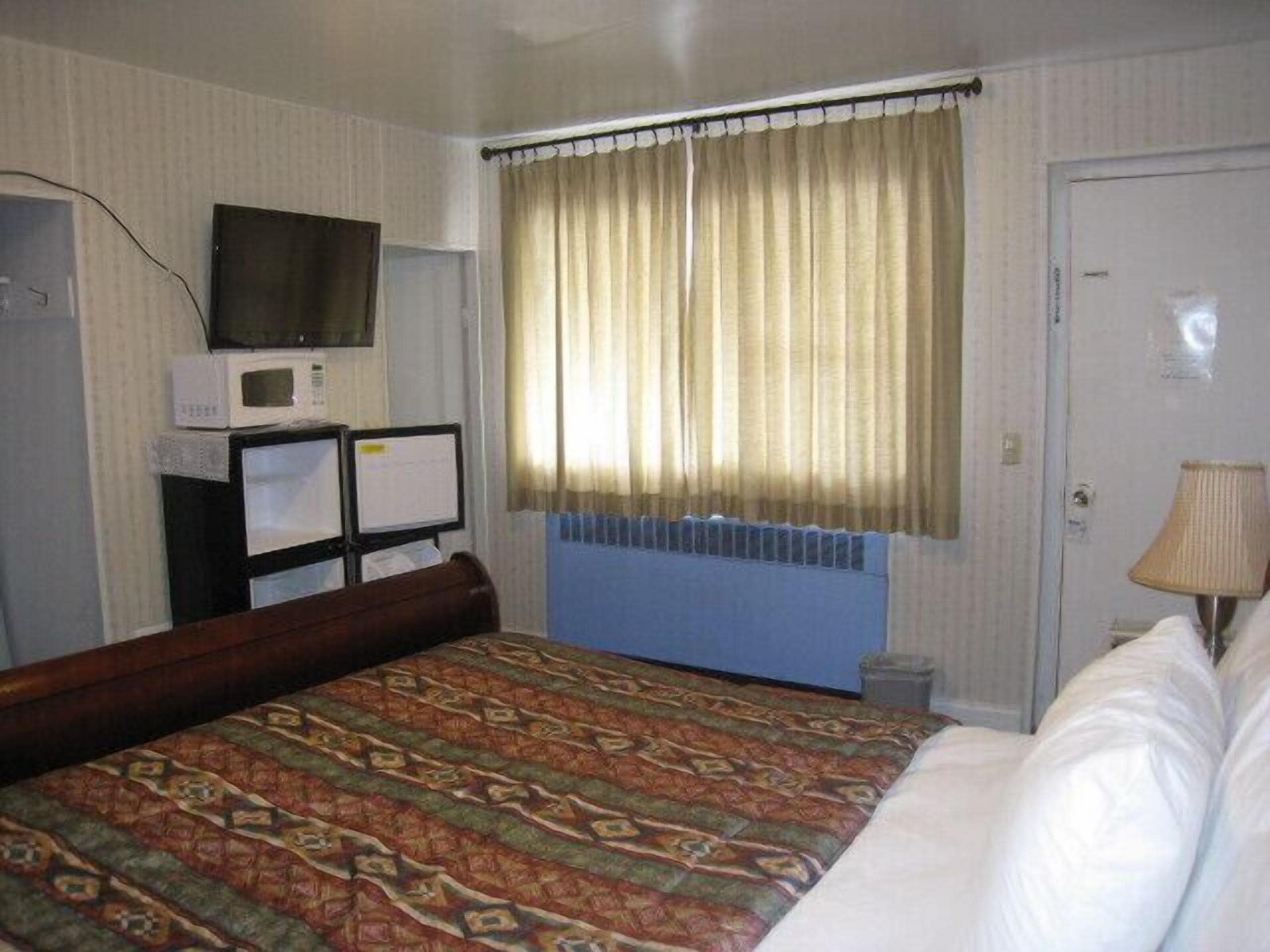 A hotel room with a bed, a television, a desk with a computer, and a window with curtains.