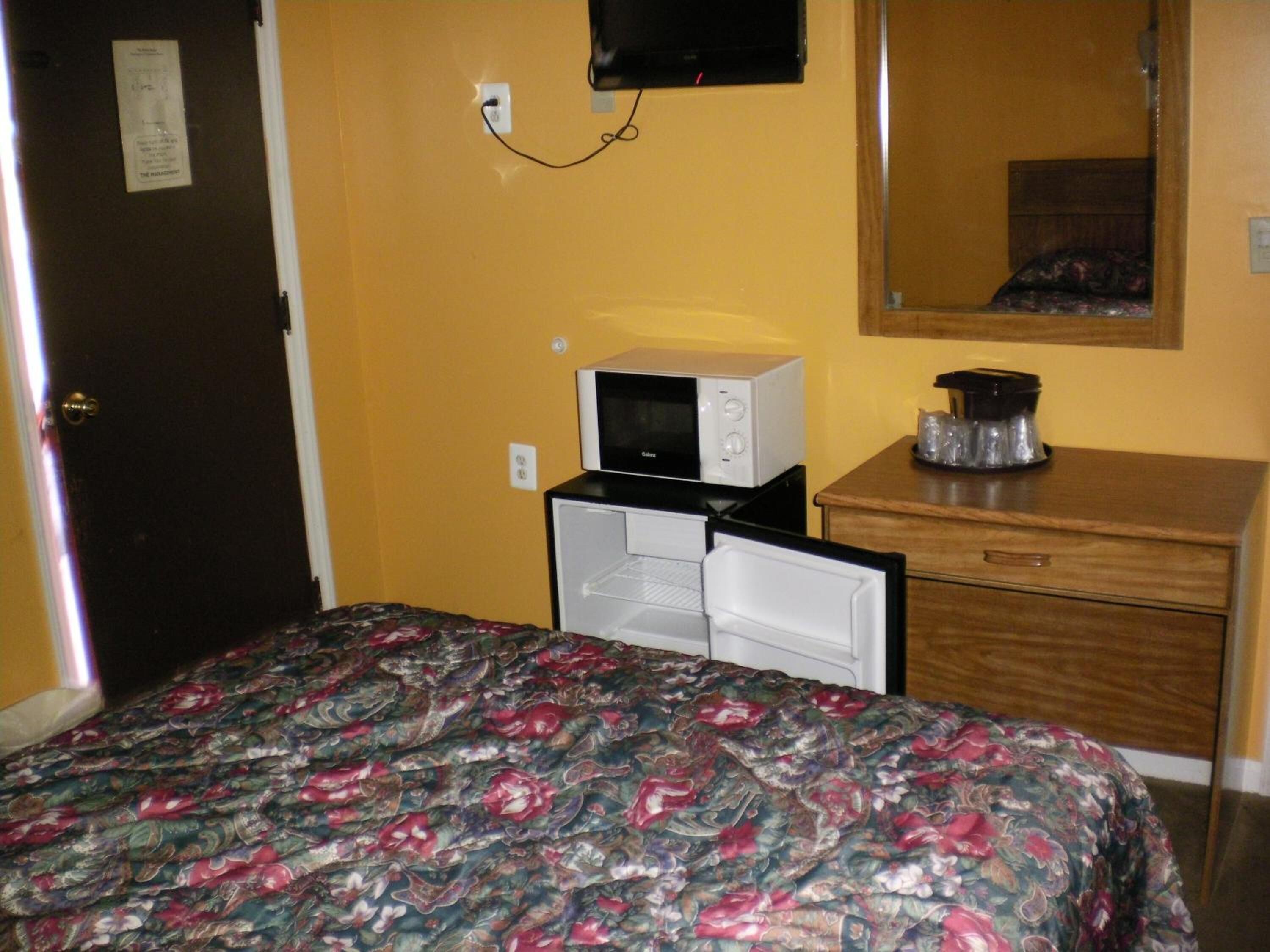 Una habitación de hotel con cama, microondas, cafetera y cómoda.