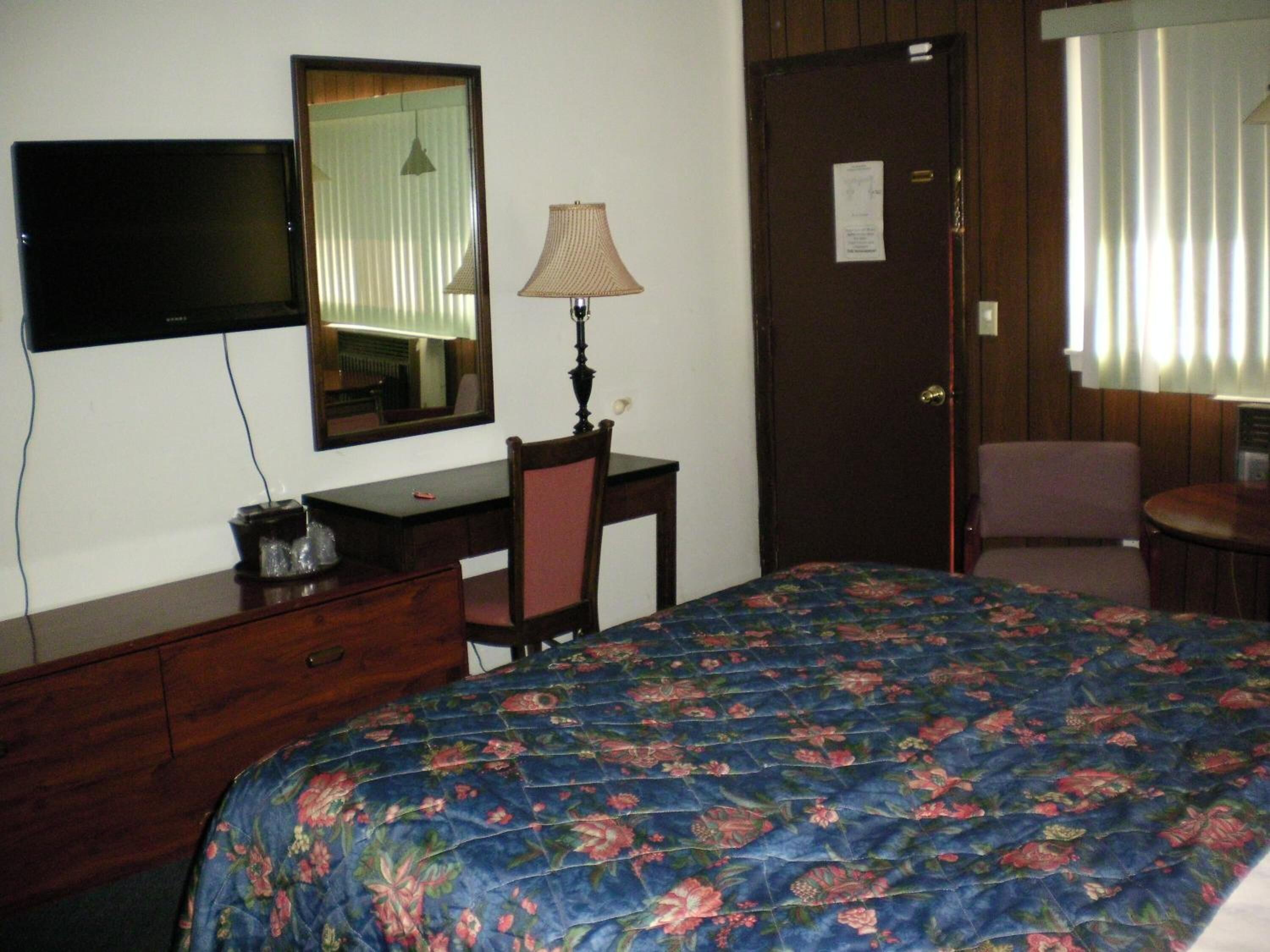 A hotel room with a bed, a desk, a chair, a television, and a door.