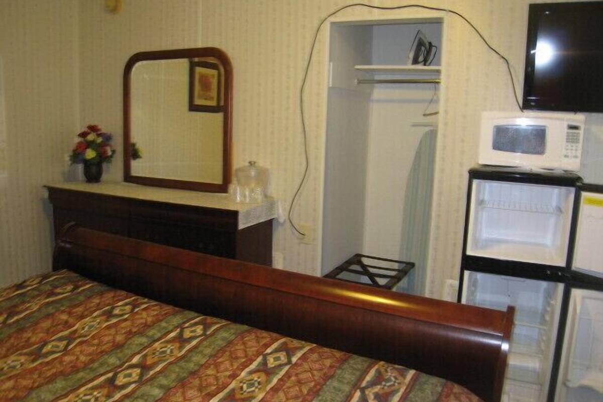 A hotel room with a bed, a dresser, a mirror, a microwave, and a closet.